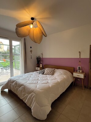 A bedroom with a large bed, a ceiling fan, a nightstand with a lamp, and a view of the outdoors through a sliding door.