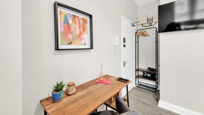 A room with a wooden table, a framed abstract painting, a coat rack, and a television. - Sunny Serenity: Studio Living with a Breeze (London)