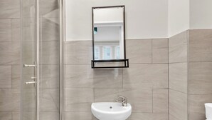 A bathroom with a glass shower enclosure, a white sink, and a mirror mounted on the wall. - Sunny Serenity: Studio Living with a Breeze (London)