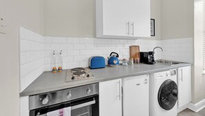 A compact kitchen with a stove, oven, washing machine, and a microwave. - Sunny Serenity: Studio Living with a Breeze (London)