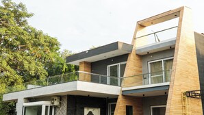 Une maison moderne à deux étages, dotée d’un balcon, de grandes fenêtres et d’une entrée avec des marches.