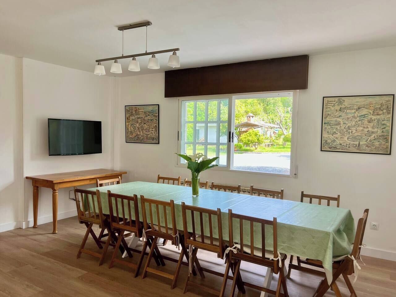 Uma sala de jantar com uma mesa comprida, cadeiras, uma televisão e obras de arte nas paredes.