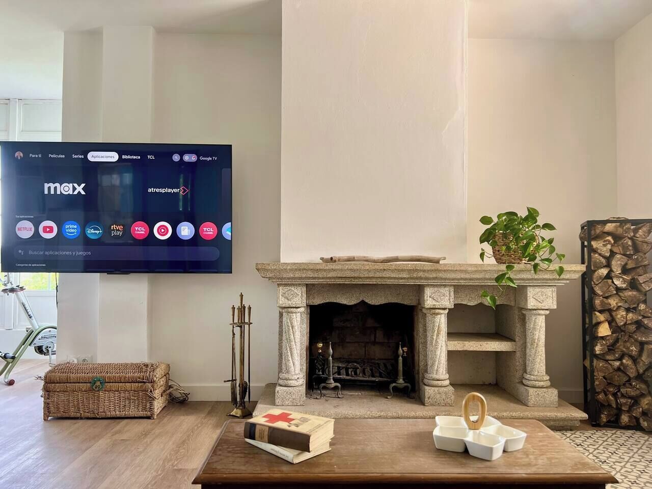 Una sala de estar con chimenea de piedra, televisor montado en la pared, una cesta de mimbre y una mesa de centro de madera.