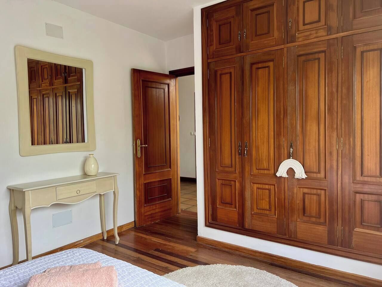 A bedroom with a bed, a bedside table, a mirror, a wardrobe, and a door leading to another room.