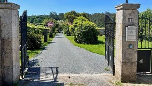 Un camino empedrado que atraviesa una entrada portonada con pilares de piedra y puertas de metal, rodeado de vegetación.