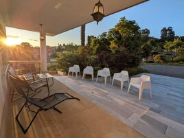 Un patio exterior con una mesa y sillas, rodeado de un jardín y vistas al atardecer.