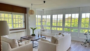 Una habitación amplia con un gran ventanal, un conjunto de sofás, una mesa de centro y una silla colgante.