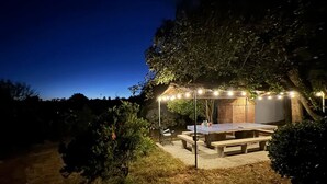 Un patio al aire libre con una mesa y bancos, rodeado de árboles y una estructura de ladrillo.