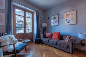 A room with a herringbone floor, a sofa, a chair, a lamp, and two framed artworks on the wall. - Saint Gervais 2 bed apart. Sleeps upto 6, Chic Period Building Central location (Saint-Gervais-les-Bains)