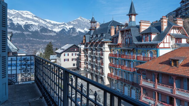 A historic building with multiple balconies, a prominent tower, and a view of snow-capped mountains. - Saint Gervais 2 bed apart. Sleeps upto 6, Chic Period Building Central location (Saint-Gervais-les-Bains)