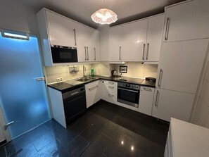 A modern kitchen with white cabinets, a black countertop, a dishwasher, an oven, and a microwave.