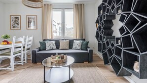A modern living room with a grey sofa, a glass coffee table, and a geometric black shelving unit. - Imperial Apartments - Andersa (Sopot)