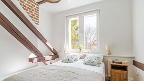 A bedroom with a bed, a window, a nightstand, and a wooden staircase. - Imperial Apartments - Andersa (Sopot)