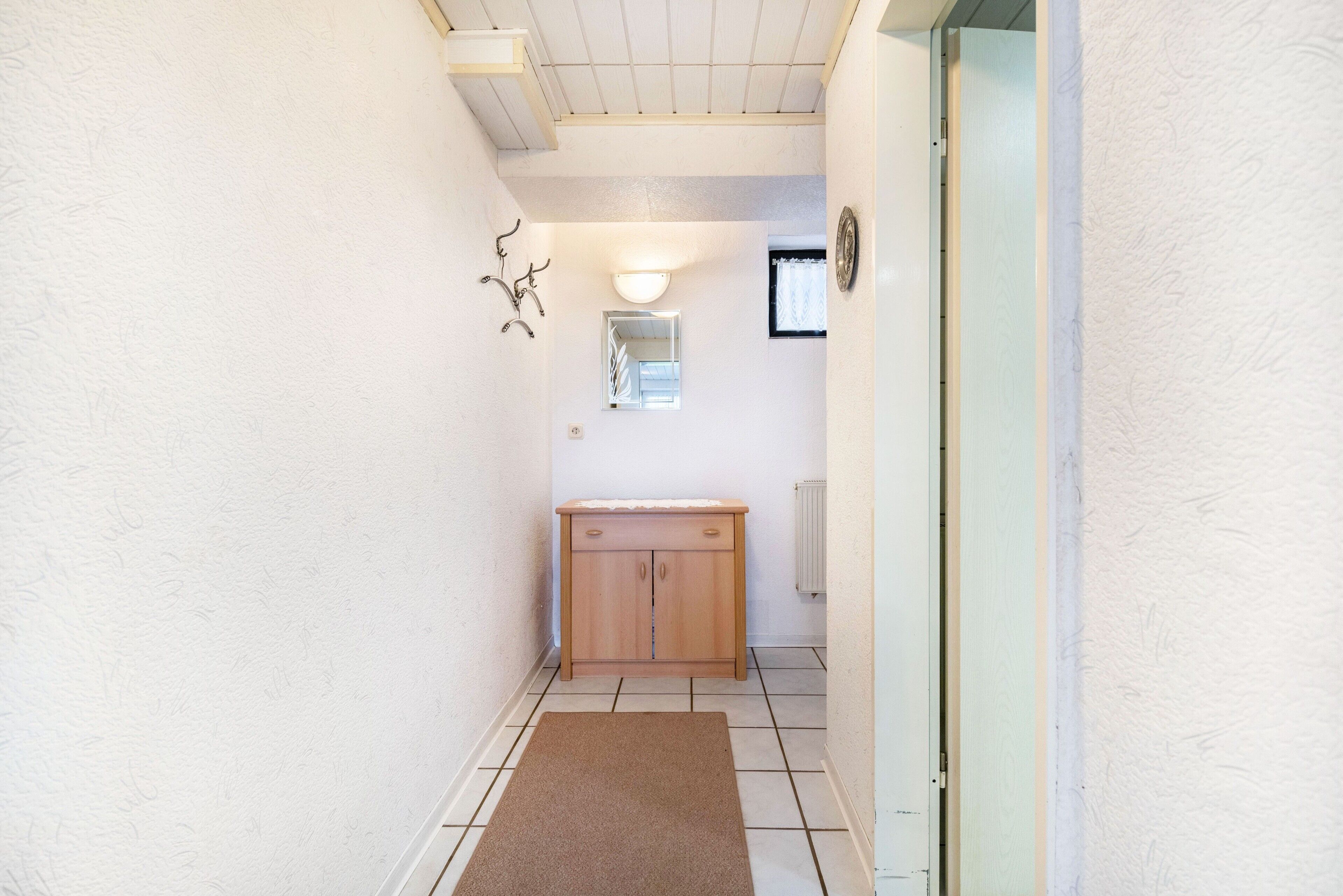 Un couloir étroit avec une armoire en bois, un radiateur et une porte donnant sur une autre pièce.