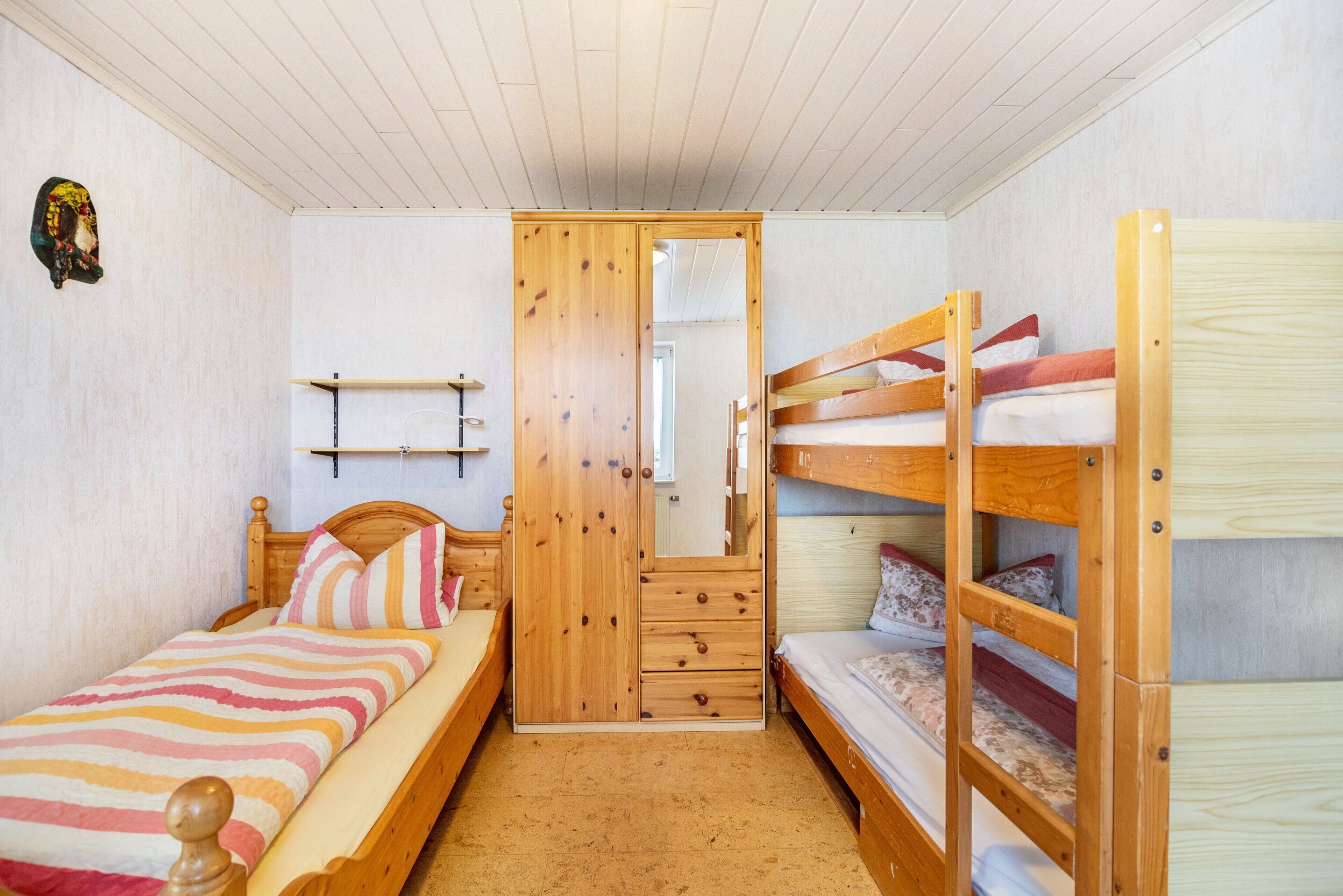 A bedroom with a single bed, a wooden wardrobe, a mirror, and a bunk bed.