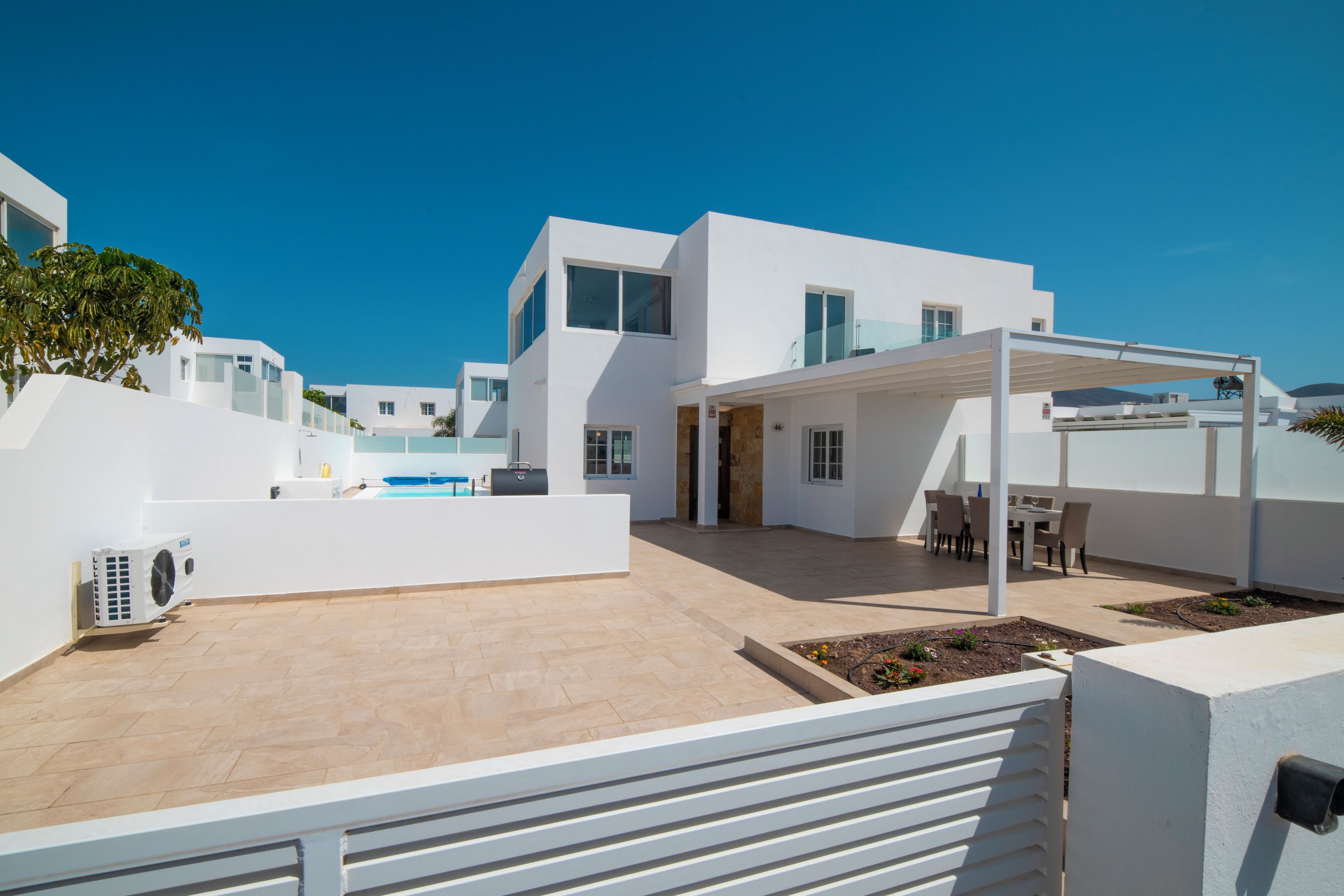 A modern white building with a covered outdoor seating area and a pool.