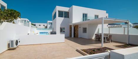 A modern white building with a covered outdoor seating area and a pool.