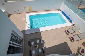 A rooftop pool with a table and chairs, surrounded by a white building. - Ocean Wave Villa-Elegant Retreat with Ocean Views and Private Heated Pool (Playa Blanca)