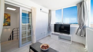 Una sala de estar moderna con un televisor, un cuenco sobre una mesa y un amplio ventanal con cortinas.