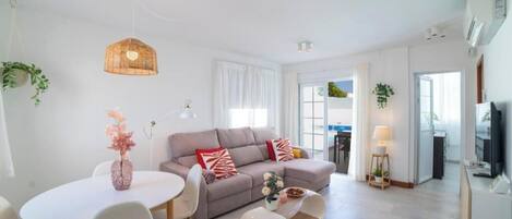 A modern living room with a sofa, dining table, and hanging light fixture.