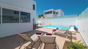 Un área de piscina exterior moderna con sillones de descanso y una pequeña mesa.