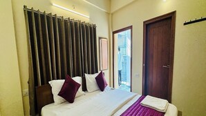 Habitación de hotel con una cama grande, cortinas oscuras, una puerta de madera y vistas al exterior.