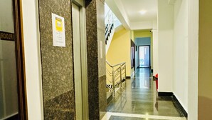 Un pasillo con piso de mármol, una escalera y una puerta con un cartel.