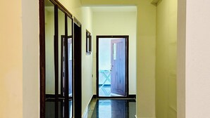 Un pasillo con una cámara, una puerta al final y una ventana a la izquierda.