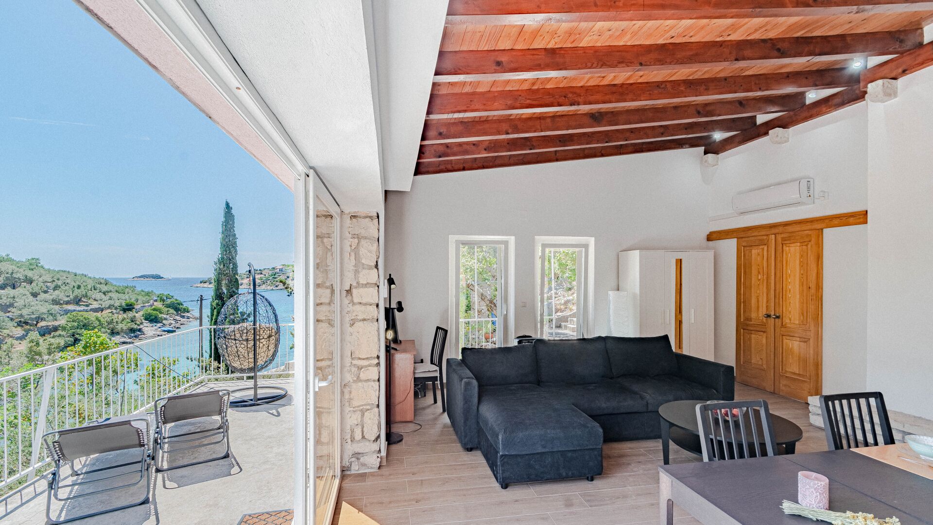 Un balcon avec vue sur la mer, un canapé noir et un plafond en bois.