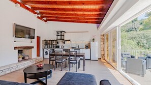 A modern kitchen with white cabinets, a dining area with a round table and chairs, a fireplace, and a balcony with wicker furniture. - Beach Escape Lujo by Villas Guide (Vela Luka)
