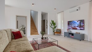 A living room with a sofa, coffee table, and a TV. There's a staircase leading to another room. - Villa  Valle Lux by Villas Guide (Bale)