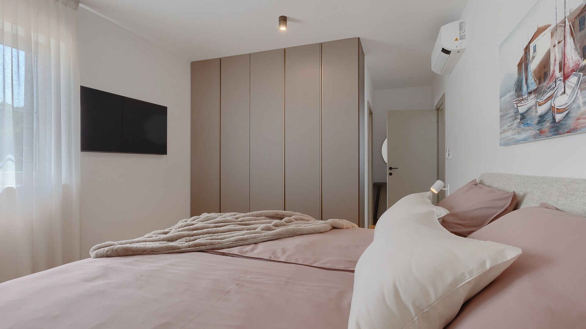 A bedroom with a bed, a TV, a painting, and an air conditioning unit.
