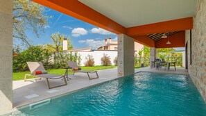 A swimming pool with lounge chairs and a table, surrounded by a garden and a building with a tiled roof. - Villa  Valle Lux by Villas Guide (Bale)