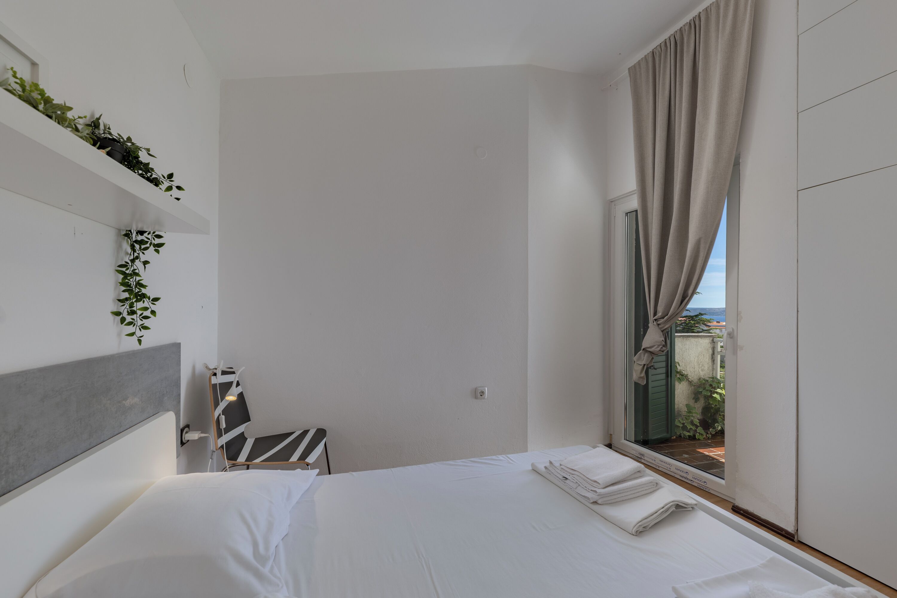 A modern hotel room with a bed, a window with curtains, a small table, and a chair.