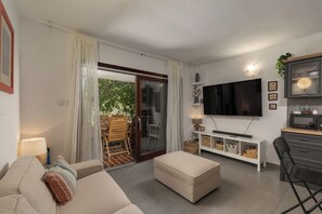 A modern living room with a sofa, ottoman, TV, and a dining area with a table and chairs.