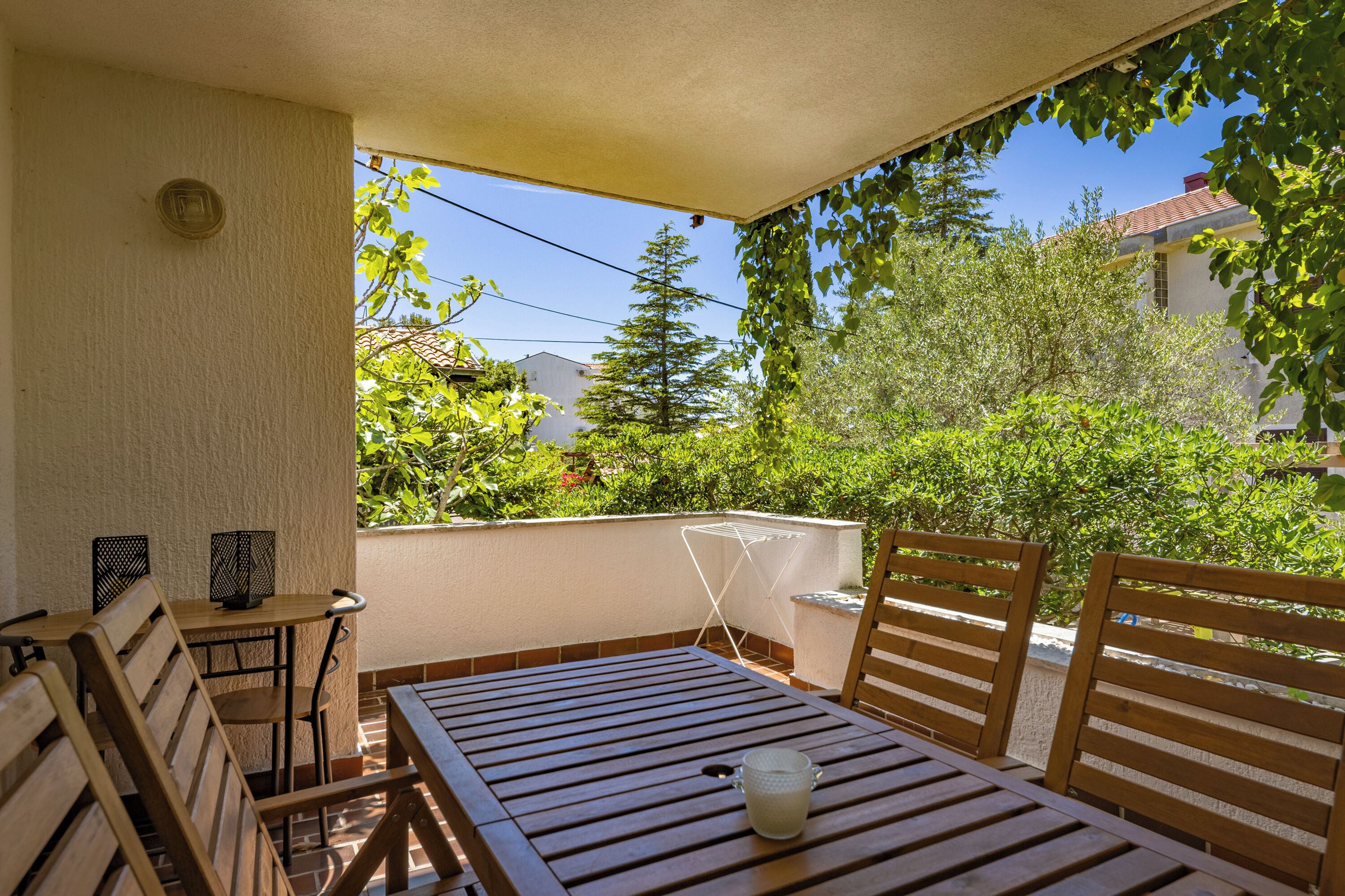 A wooden table and chairs on a balcony with a view of greenery and buildings.