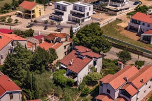 An aerial view of a residential area with modern houses, a road, and surrounding greenery. - Punta Debij Apartments (Punat)