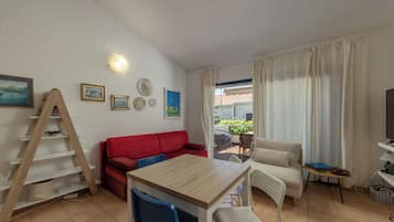 A furnished living room with a wooden table, two sofas, a TV, and a balcony with plants.