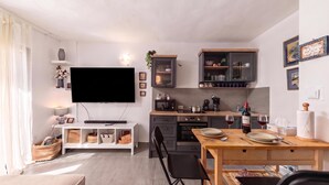 A modern kitchen with a flat-screen TV, wooden cabinets, and a dining area with a table and chairs. - Punta Debij Apartments (Punat)