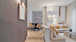 Una sala de estar moderna con un sofá, una mesa de comedor con sillas y una escalera que sube a otro nivel.