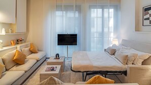 Una habitación de hotel moderna con sofá, cama, televisión y mesita de noche.