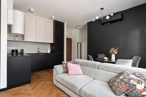 Une cuisine moderne avec des meubles blancs, un plan de travail noir et un canapé gris agrémenté de coussins à motifs floraux.