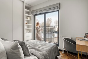 A bedroom with a bed, a desk, a chair, a window with a view of trees, and a built-in wardrobe. - Art Deco Mokotów Suites - Parking & Gym by Downtown Apartments (Warszawa)