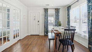 A room with a dining table, chairs, a door, and large windows with curtains. - Midtown 3-bedroom house in vibrant Tulsa close to TU, Downtown, EXPO Square (Tulsa)
