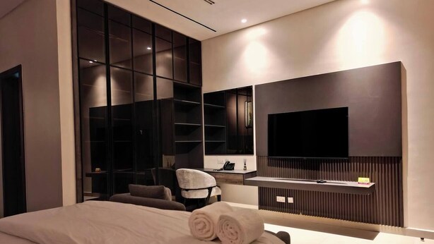 A modern bedroom with a large bed, a TV, and built-in storage. - The Zeal Luxury Apartment  (Benin City)