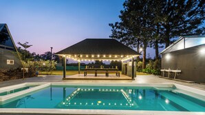 Une piscine dotée d’un espace détente couvert et illuminé de guirlandes lumineuses.