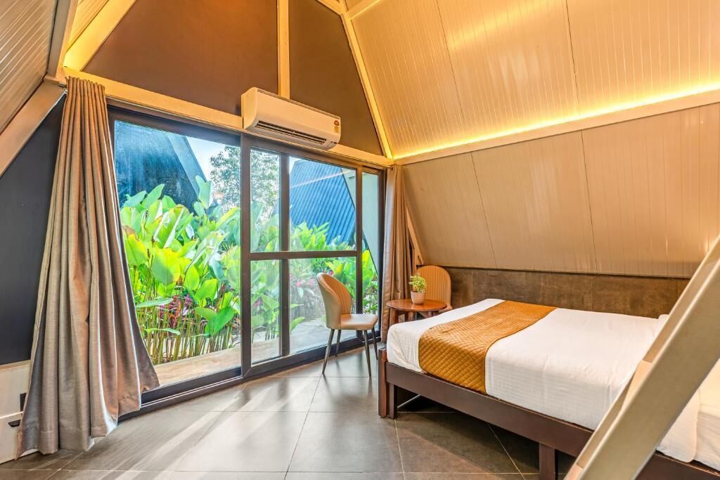 Una habitación con cama, una silla, una mesita y un ventanal con cortinas.