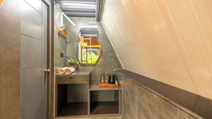 Un couloir étroit avec un miroir, un porte-serviettes et une petite étagère sur laquelle se trouvent des bouteilles et une bouilloire.