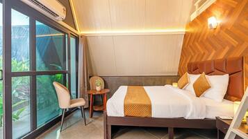 A hotel room with a bed, a chair, a small table, and a window with a view of greenery.