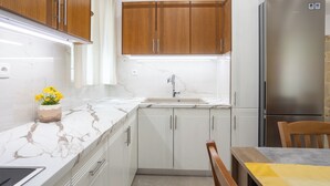 Une cuisine avec des meubles de rangement en bois, un réfrigérateur en acier inoxydable, un plan de travail en marbre et un évier.